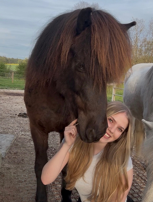 Sophia vom IPZV-Bayern lächelt glücklich neben ihrem kuscheligen Pferd.